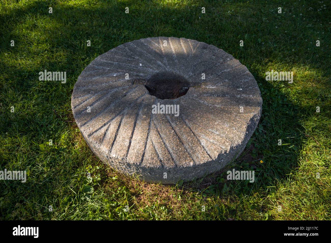 Macina per grano macinando o grani altri. Macinando pietre. Vecchio elemento di mulino su erba verde Foto Stock