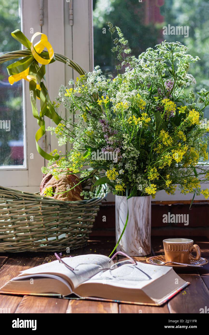 Prati Fiori in vaso, cestino di vimini, pane aggiungere intimità foto verticale del paese estivo stile di vita. Fuoco selettivo all'aperto. Foto Stock