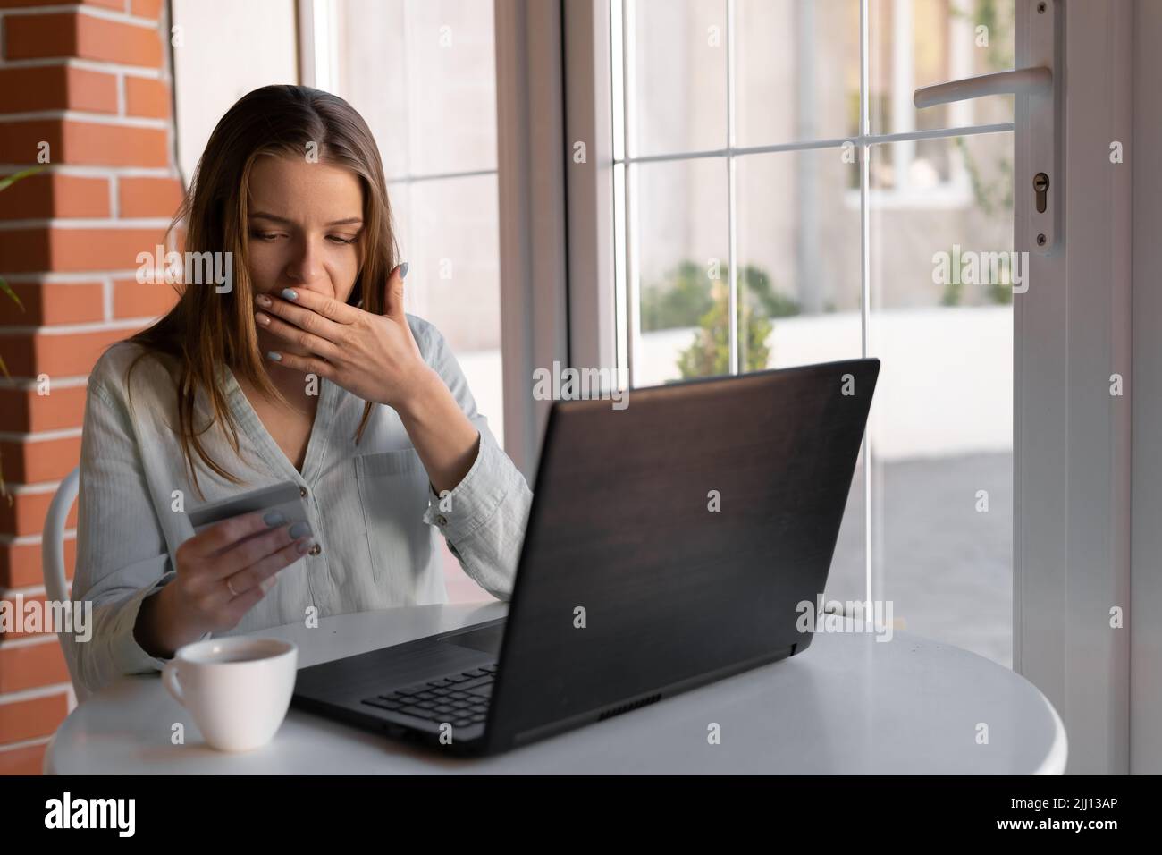 Donna preoccupata che ha difficoltà a pagare online con carta di credito e laptop al caffè. La mano della donna che tiene carte di credito, la sensazione di stress su tasse e debito Foto Stock