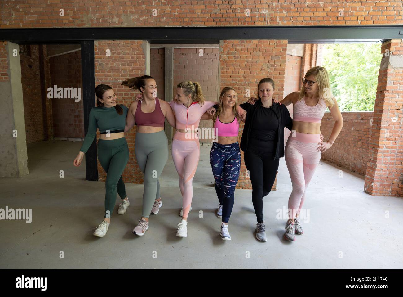 Gruppo di amici femminili in forma di diversi tipi di corpo in abbigliamento sportivo che camminano braccio in braccio insieme e divertirsi dopo una lezione di allenamento in palestra. Foto di alta qualità Foto Stock