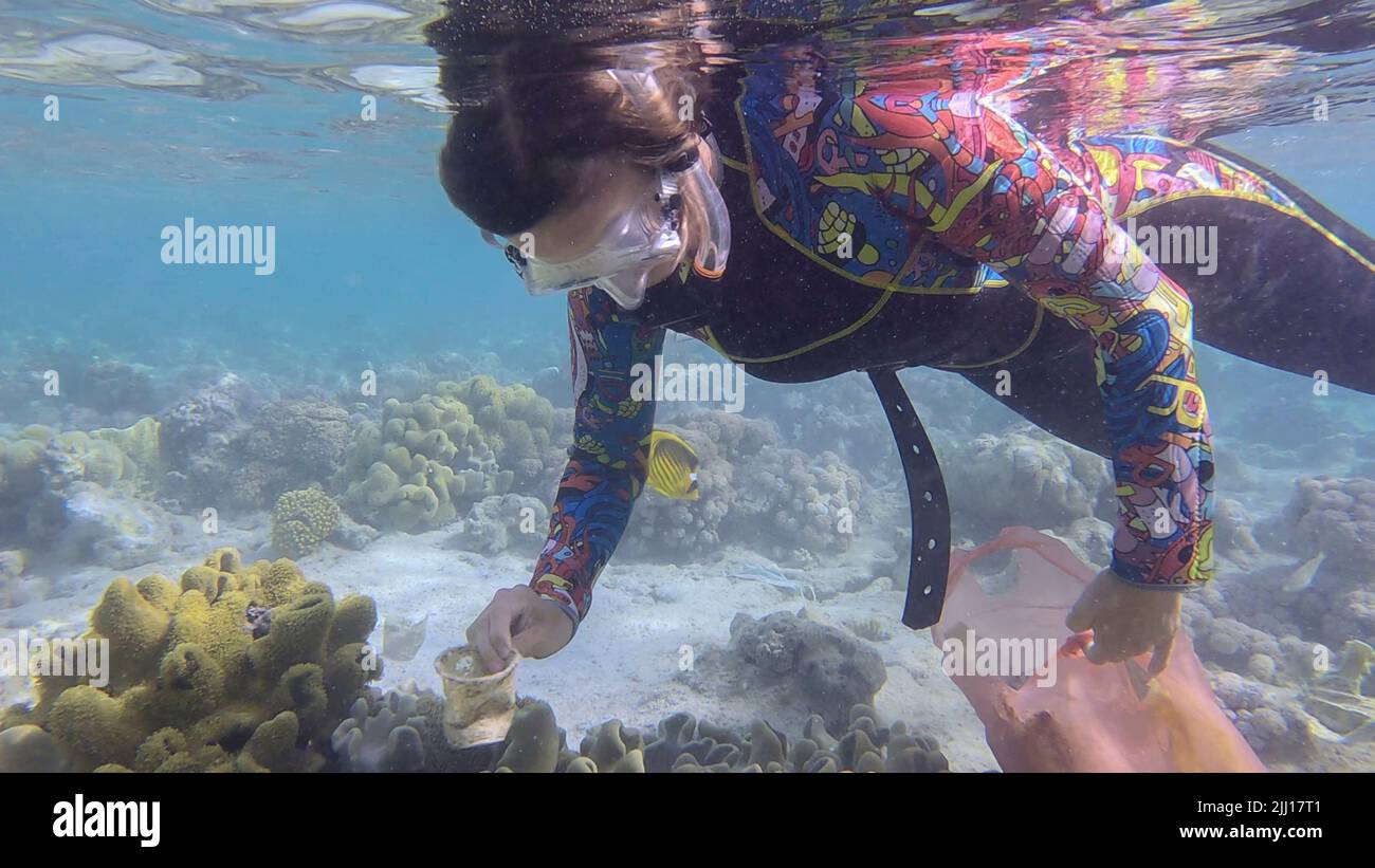 La donna in attrezzatura subacquea nuota e raccoglie i detriti di plastica sott'acqua sul fondo della barriera corallina. Lo snorkeler pulisce l'Oceano dall'inquinamento di plastica. P Foto Stock