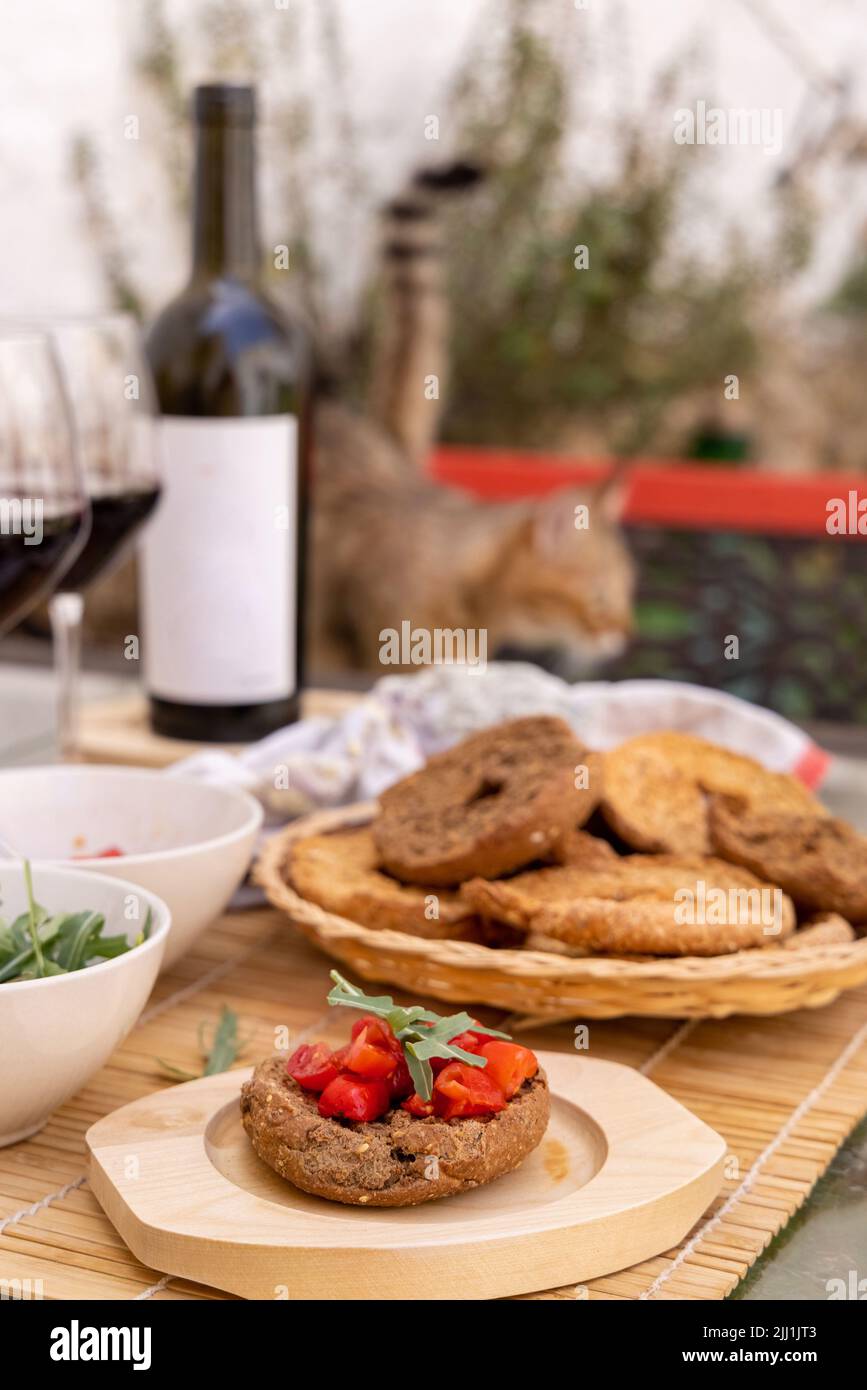 Antipasto estivo italiano Friselle con pomodori ciliegini, olio e rucola serviti all'aperto con bicchieri di vino rosso. Pane secco tipico della Puglia, prodotto in S. Foto Stock