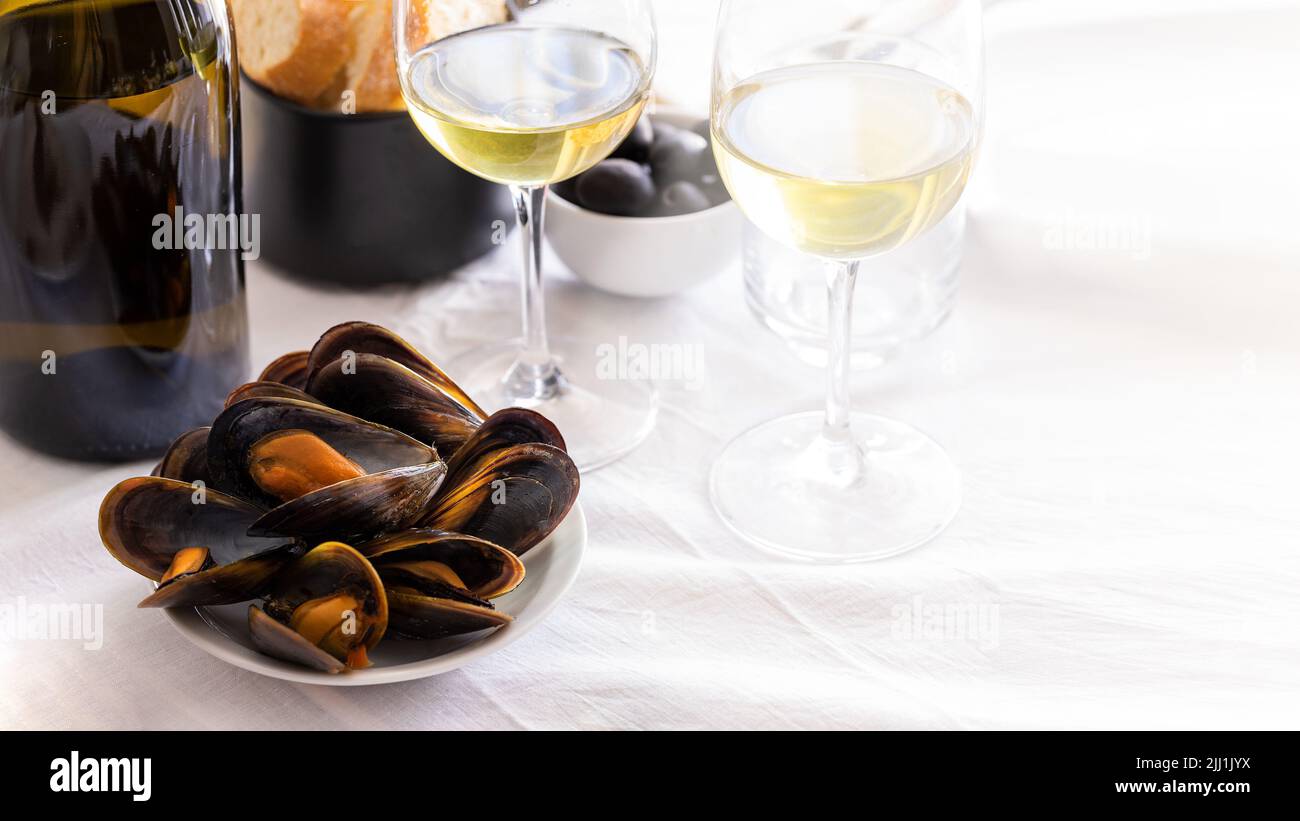 Cozze al vapore con un bicchiere di vino sul tavolo del ristorante. Tipico sfondo mediterraneo.spazio copia. Foto Stock