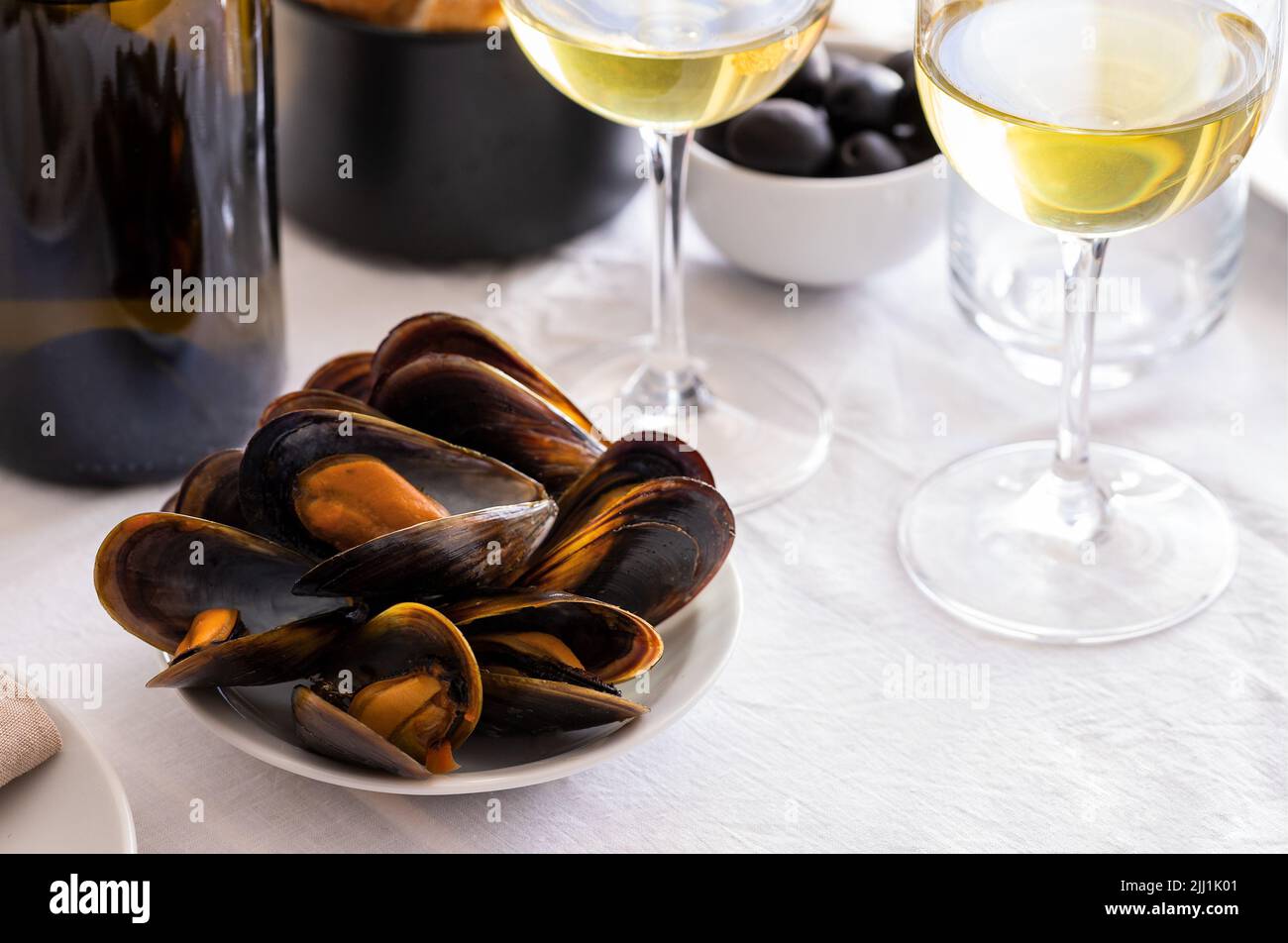 Cozze al vapore con un bicchiere di vino sul tavolo del ristorante. Piatto tipico mediterraneo Foto Stock
