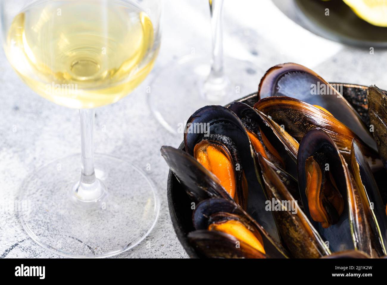Cozze al vapore servite in padella, bicchieri di vino bianco su fondo cementizio. Popolare sfondo di piatti mediterranei di pesce. Foto Stock