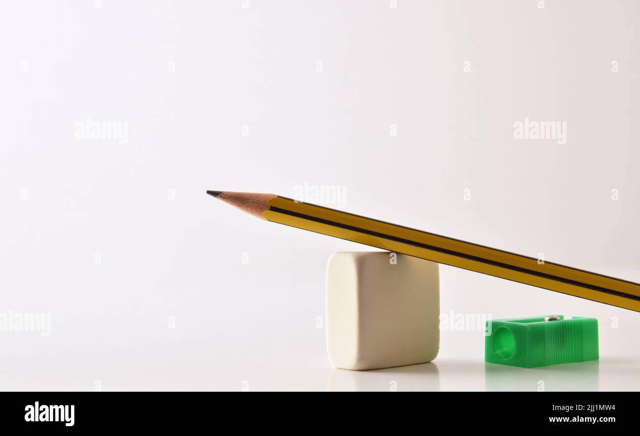 Fondo concettuale di base dell'insegnamento nelle scuole con matita, cancellatore e affilatore sul tavolo e sfondo bianco isolato. Vista frontale. Foto Stock