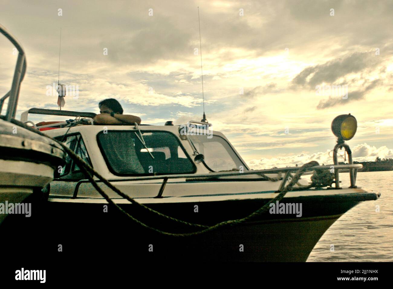 Un autista di barca che controlla mentre è in piedi dietro il volante di un motoscafo che è ormeggiato ad un'altra barca ad un molo sul lato del fiume Segah in Tanjung Redeb, Berau, Kalimantan orientale, Indonesia. Foto Stock