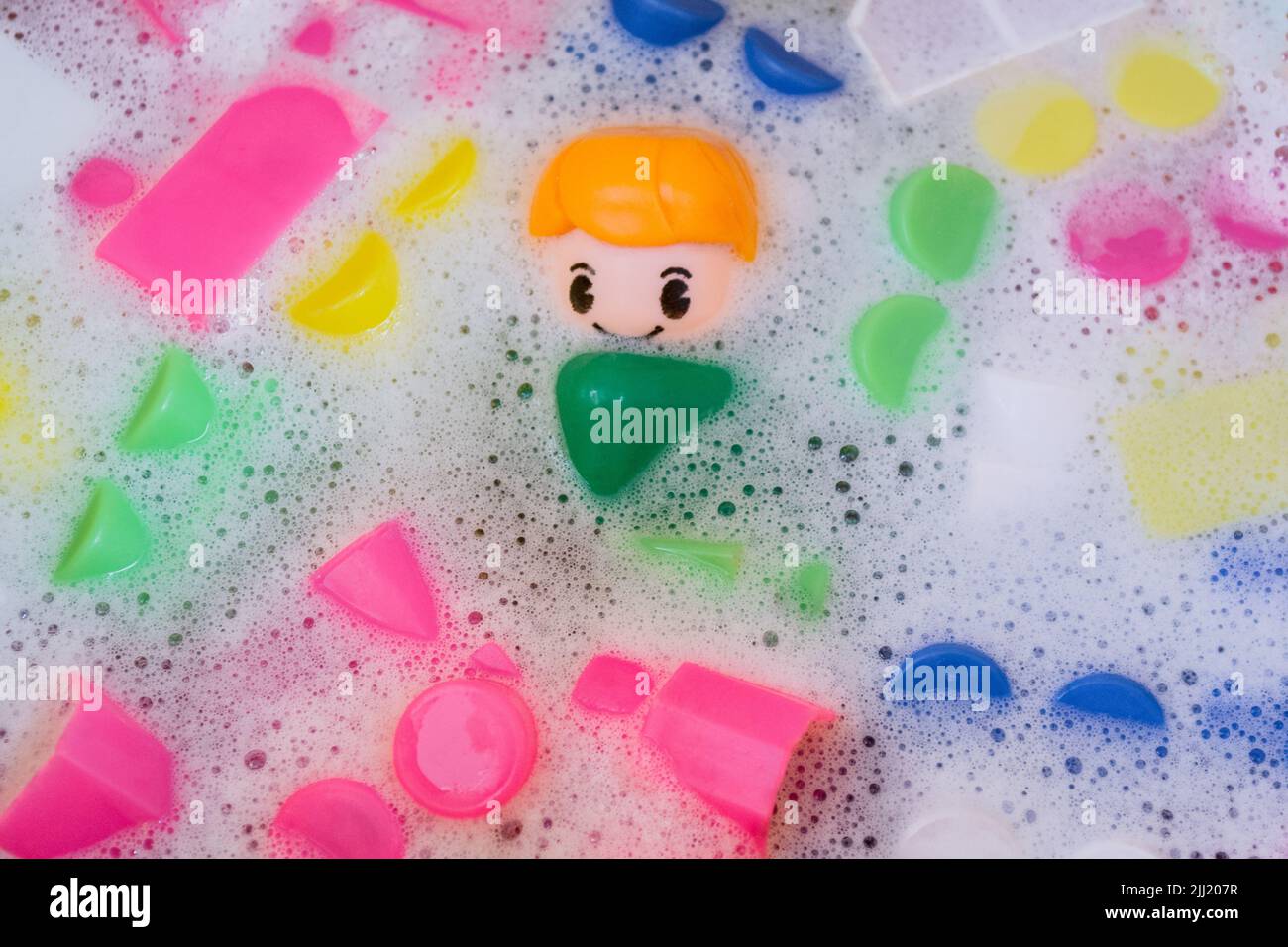 Lavaggio di giocattoli per bambini, blocchi da costruzione in plastica con figurine. Un piccolo compagno sorridente e cubi colorati galleggiano nell'acqua schiumosa. Foto Stock