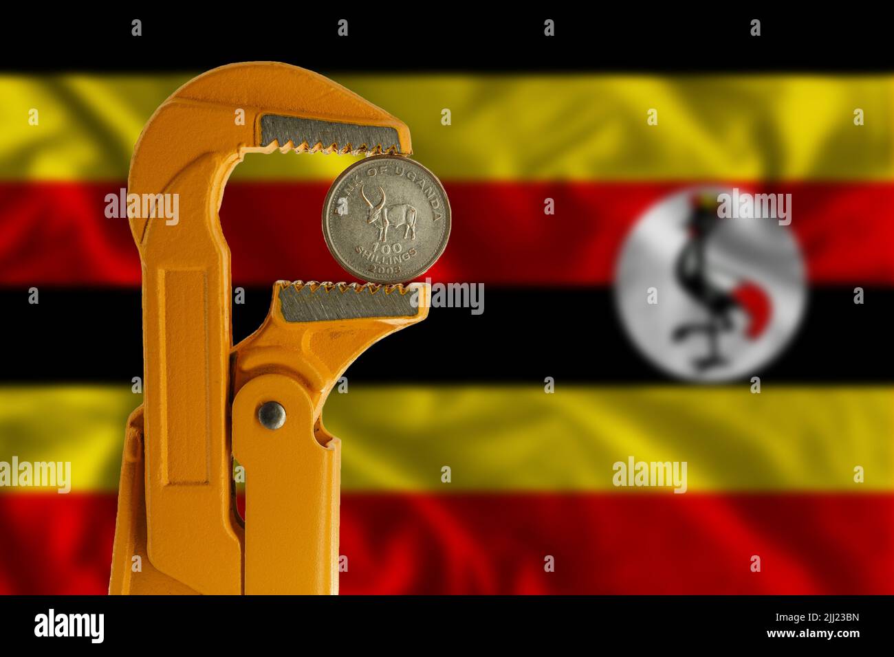 Cento scellini di moneta ugandese tenuti in una chiave per idraulico arancione sullo sfondo della bandiera ugandese. Foto Stock