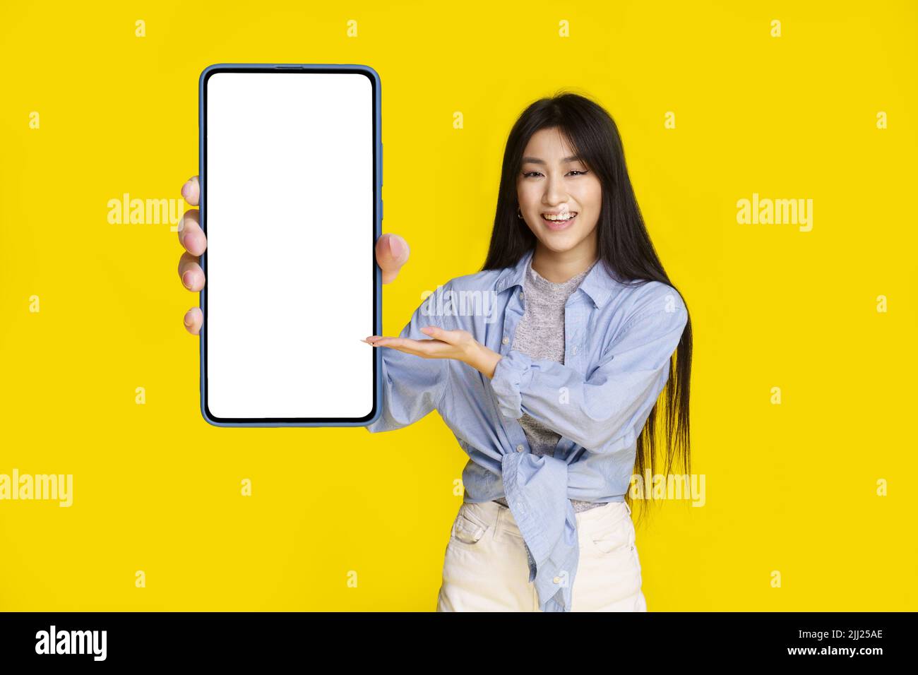 Bella ragazza asiatica con smartphone con schermo bianco felice di introdurre nuova app, gioco, vincere, isolato su sfondo giallo. Posizionamento del prodotto. Pubblicità app mobile. Foto Stock