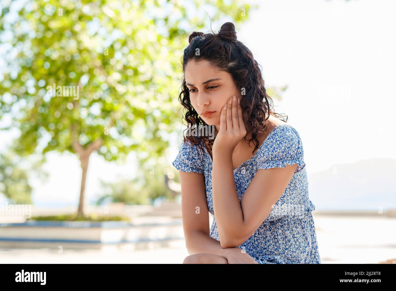 Bella donna bruna indossando abito estivo in piedi sul parco della città, all'aperto toccando la bocca con la mano con espressione dolorosa a causa di mal di denti o. Foto Stock
