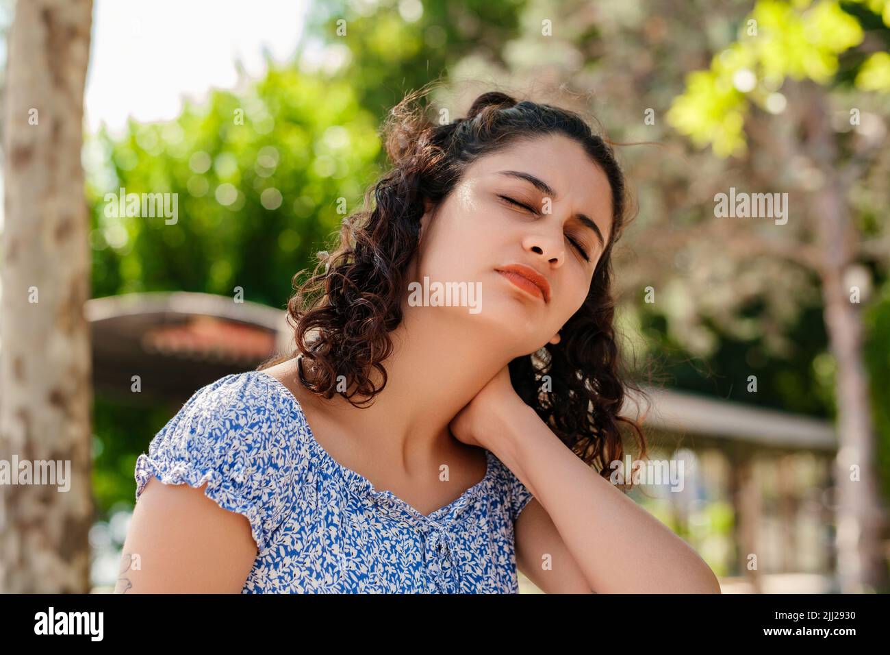 Bella donna bruna vestito estate in piedi sul parco della città, all'aperto sensazione di ferita alle spalle articolare dolore alla schiena, concetto di fibromialgia, vicino Foto Stock