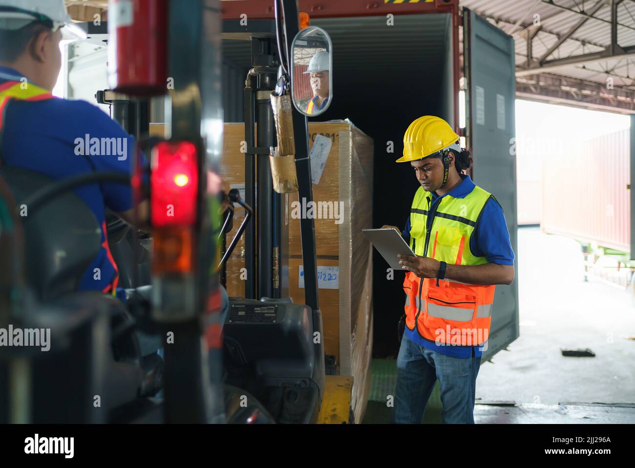 Conducente carrello elevatore asiatico che carica un contenitore di carico di spedizione con un pallet completo con le scatole nel terminal del porto logistico. Il lavoratore di magazzino asiatico e la sicurezza i Foto Stock