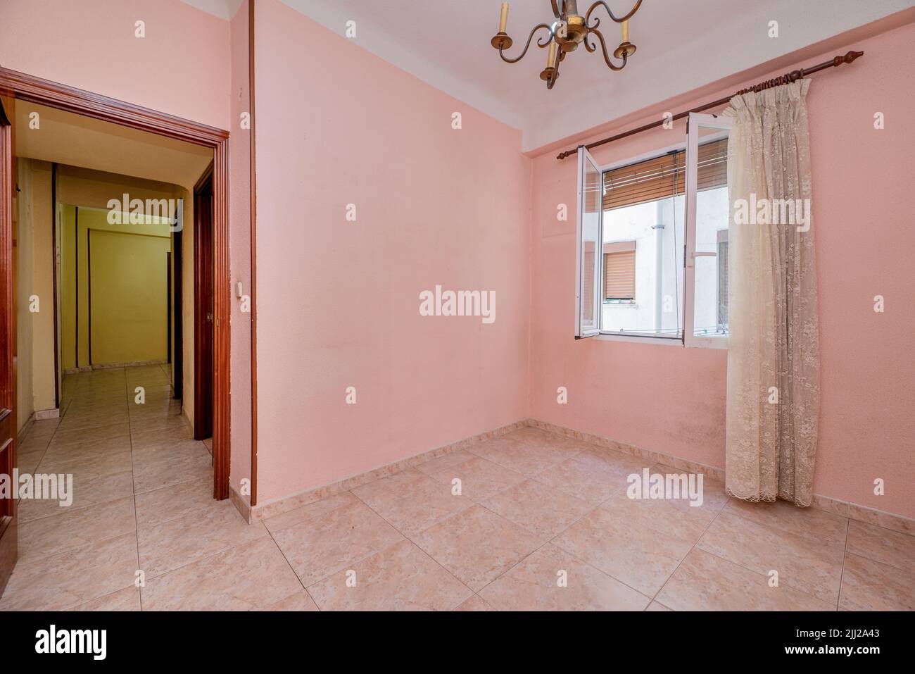 Camera vuota con pavimento in gres rosa, pareti dipinte di rosa e legno abbinato e finestra con tende bianche Foto Stock