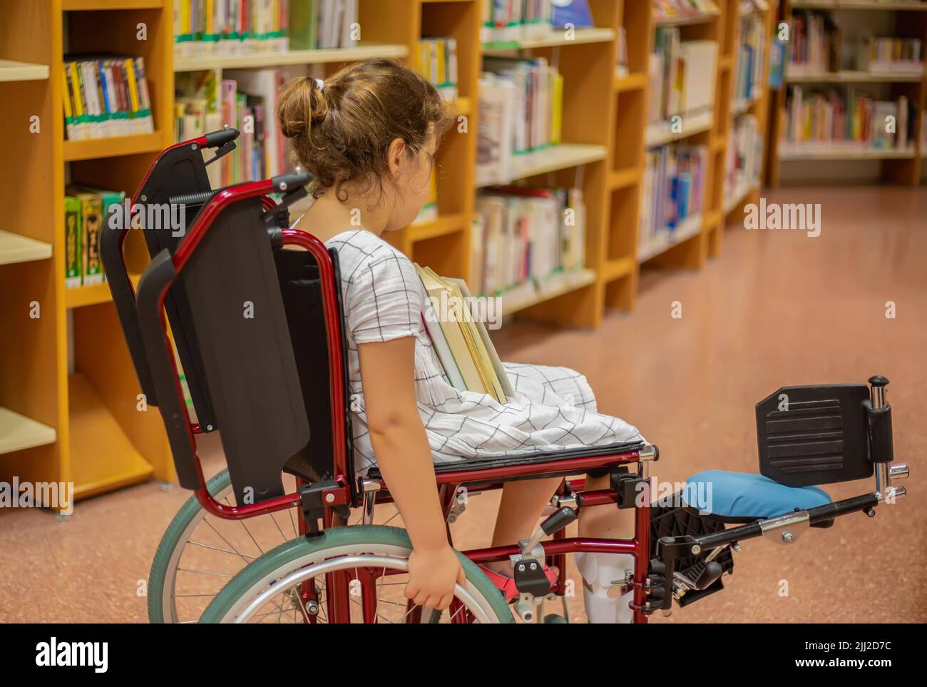 Una studentessa in una sedia a rotelle sceglie i libri nella biblioteca.vita all'età di istruzione dei bambini con bisogni speciali.concetto di istruzione di un felice Foto Stock