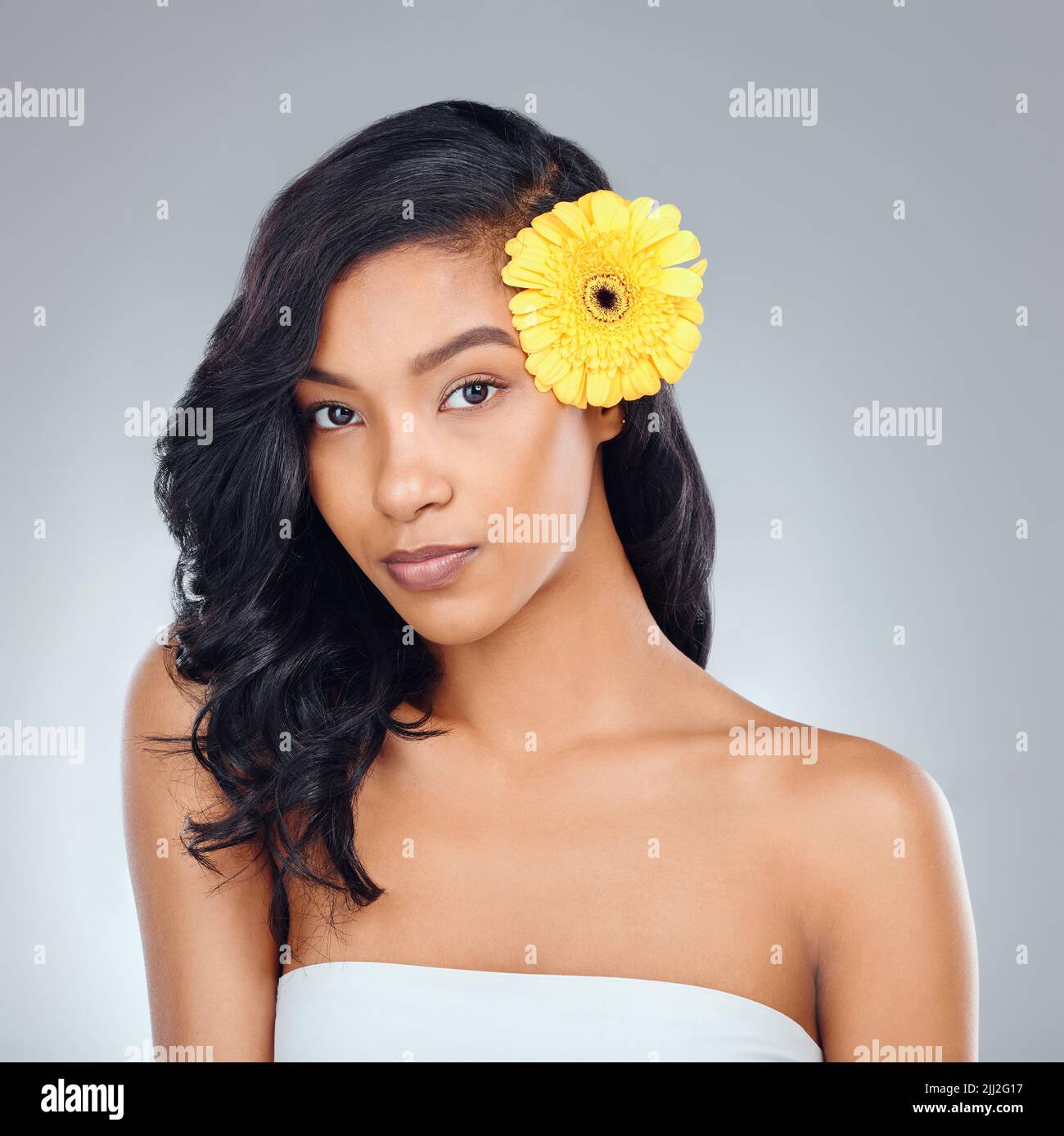 Tutti i fiori sono belli a loro modo, come anche le donne. Studio ritratto di una giovane donna attraente in posa con un fiore giallo nei suoi capelli Foto Stock