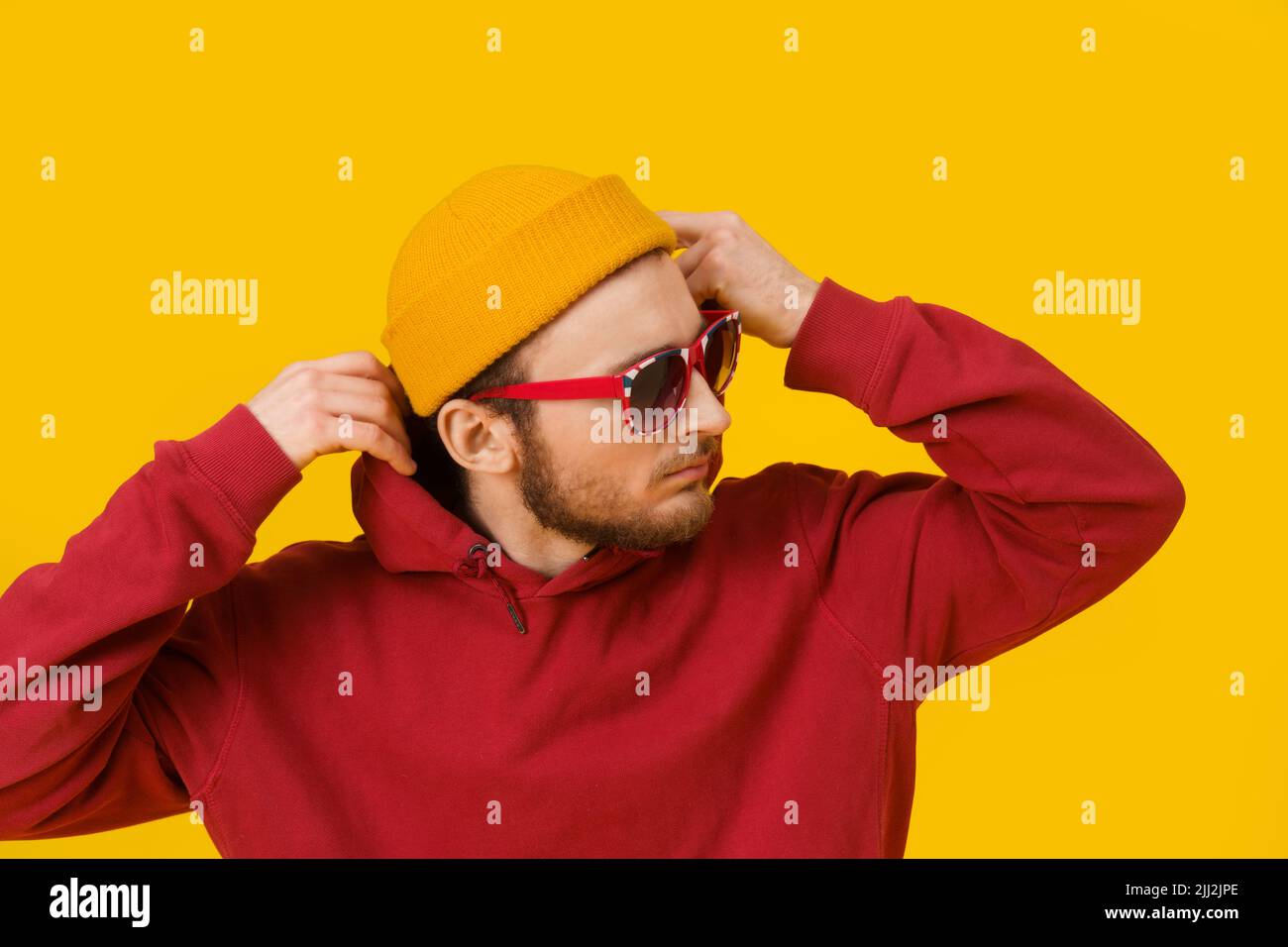 Primo piano ritratto del giovane uomo pensivo in abbigliamento casual in occhiali da sole che si posa lateralmente su sfondo giallo. Elegante look casual da uomo hipster dal bearded elegante. Ragazzo premuroso su sfondo giallo. Foto Stock