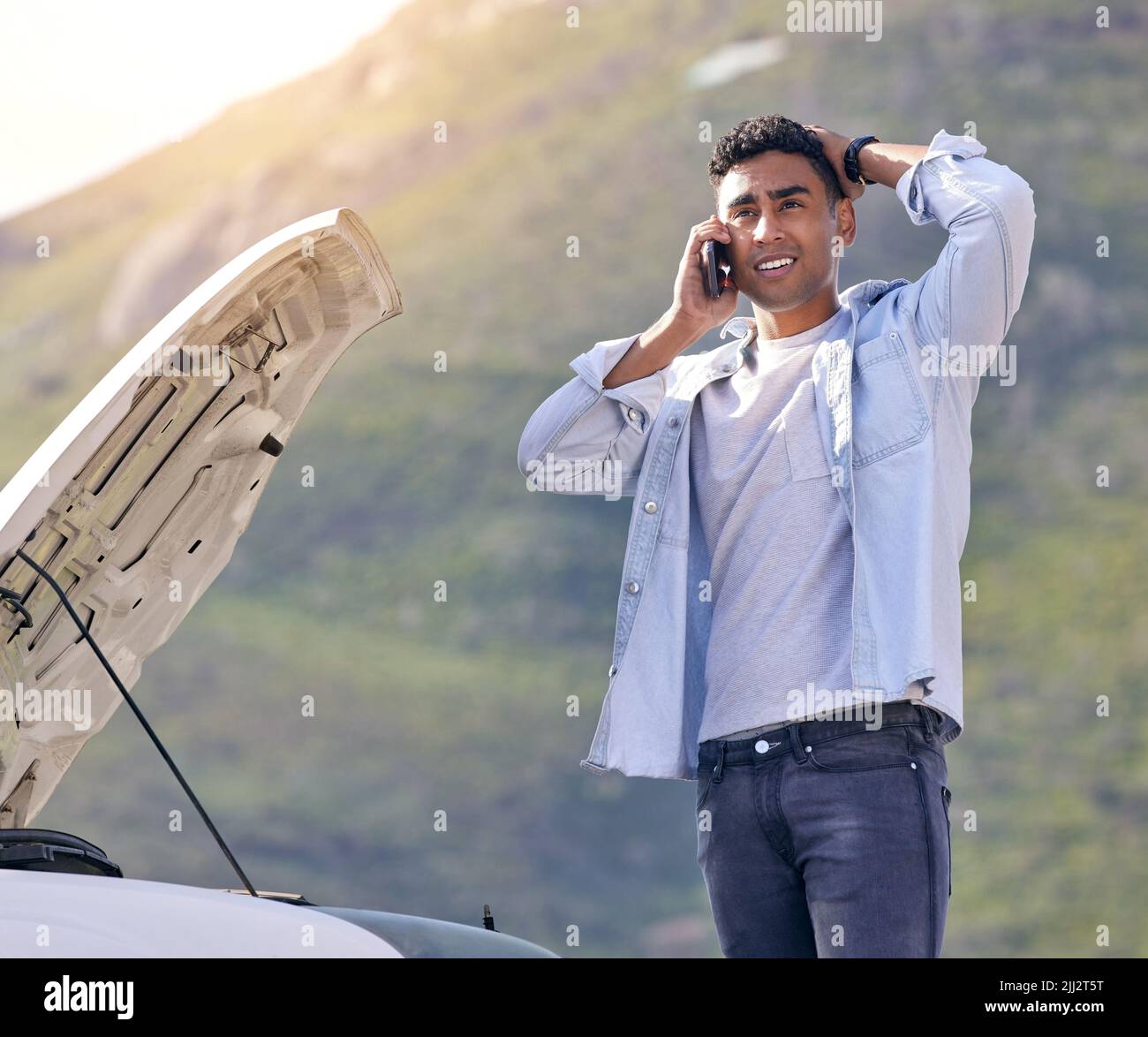 La mia auto si è appena rotta. Un bel giovane al telefono con assistenza stradale dopo aver subito un guasto al veicolo. Foto Stock