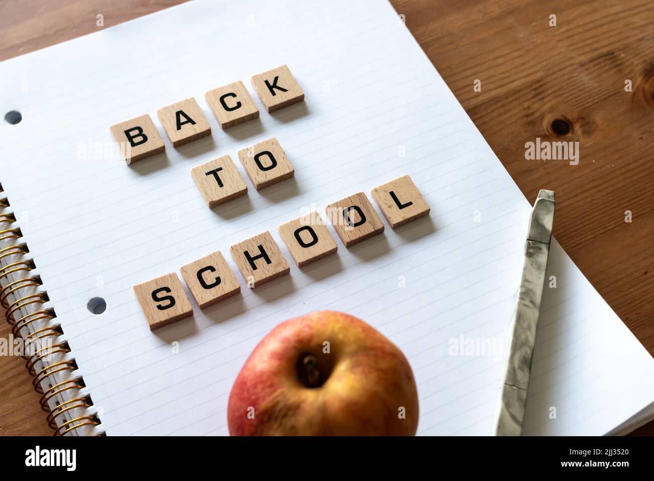 Le lettere di legno spiegano "ritorno a scuola" su un blocco note bianco rivestito accanto a una mela rossa e a una penna. Superficie della scrivania in legno duro. Apprendimento. Foto Stock