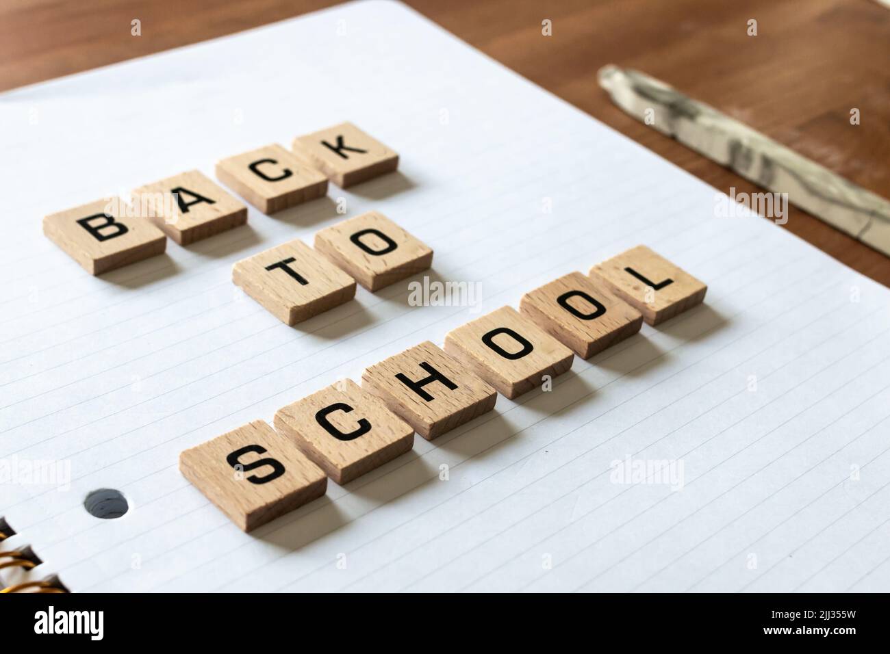 Le lettere di legno spiegano "ritorno a scuola" su un blocco note bianco rivestito accanto a una mela rossa e a una penna. Superficie della scrivania in legno duro. Apprendimento. Foto Stock