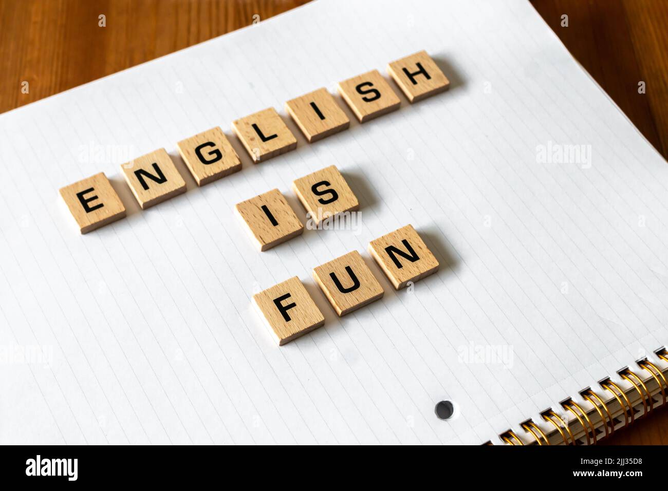 Le lettere di legno spiegano "l'inglese è divertimento" su un blocco note bianco rivestito. Superficie della scrivania in legno duro. Ritorno a scuola, apprendimento di persona, apprendimento online. Foto Stock