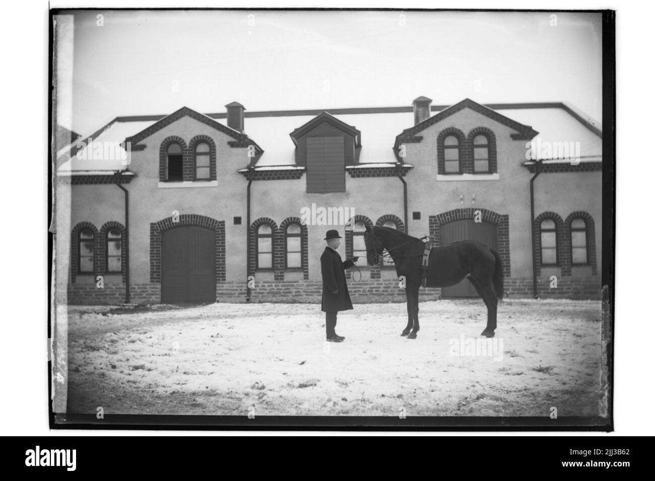 Edificio stabile di un piano e mezzo in mattoni e intonaco a corda. Un uomo e un cavallo. Distributore di cavalli N. Nilsson Foto Stock