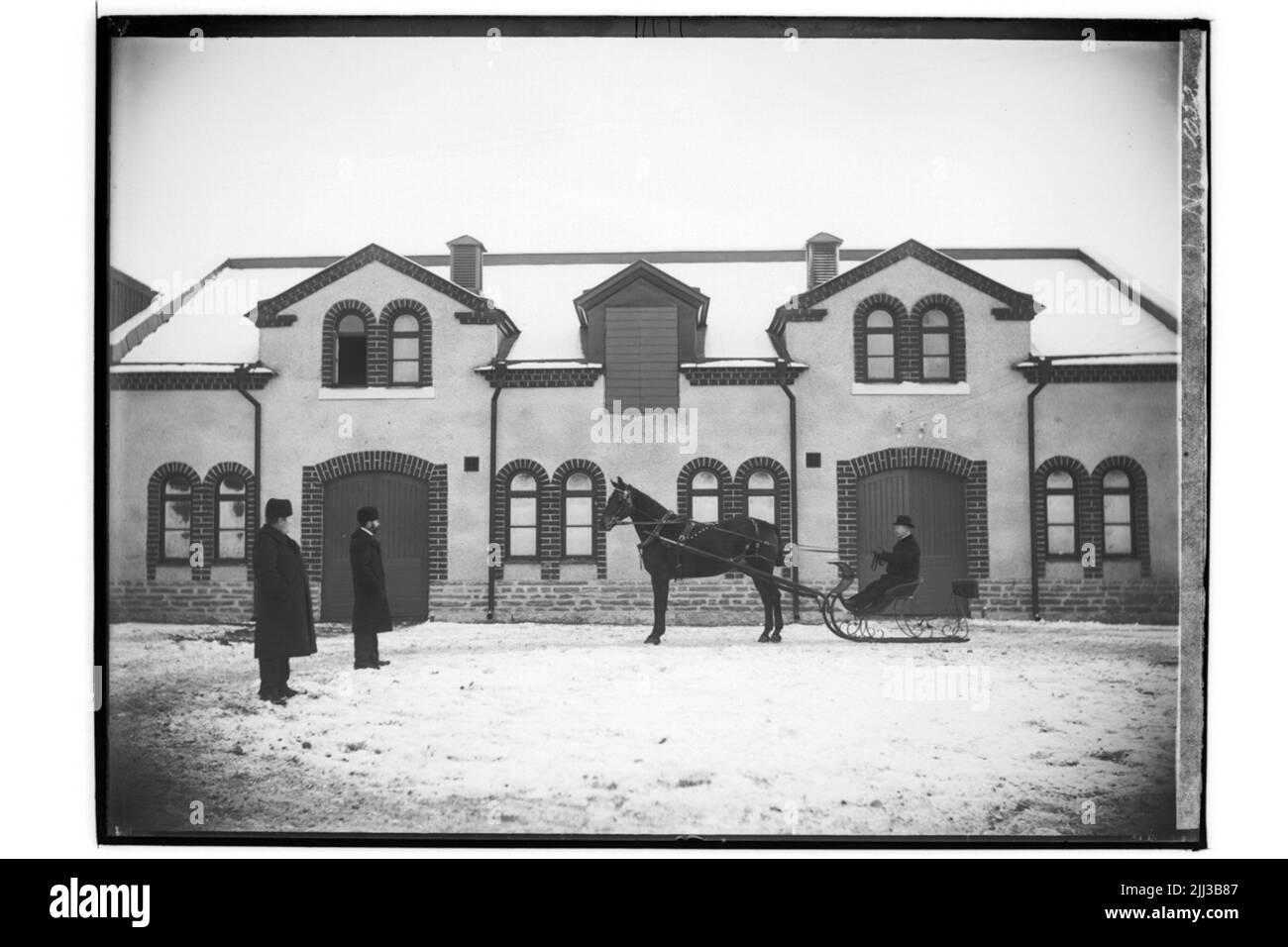 Edificio stabile a un piano e mezzo. Tre persone e un cavallo con slitta. Distributore di cavalli N. Nilsson Foto Stock