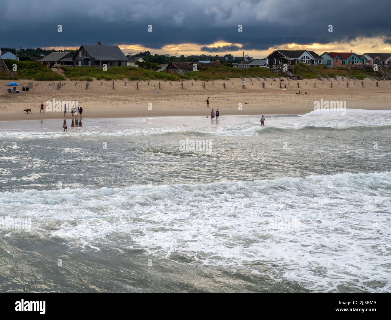 I turisti si guazzano e guardano le nuvole di tempesta e le grandi onde, effetti delle fasce esterne di un uragano al largo della costa atlantica. Foto Stock