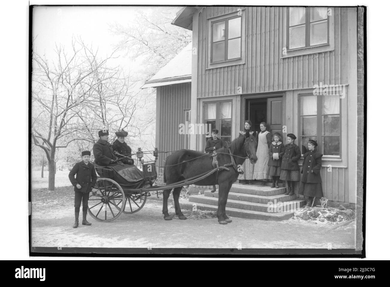 Edificio residenziale a un piano, con vento arredato e stufa frontale. Cavallo teso per un concerto con 2 persone in. 7 persone di fronte alla casa. Chiesa Pastore Gustaf Pettersson Foto Stock