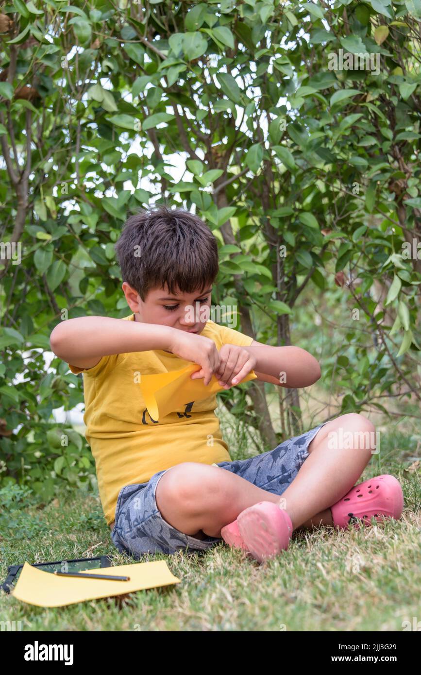 Ragazzo che gioca a filo piano di carta all'aperto guardando via. Ritratto di un allegro ragazzo caucasico che gioca in primavera e parco estivo divertirsi sul Foto Stock