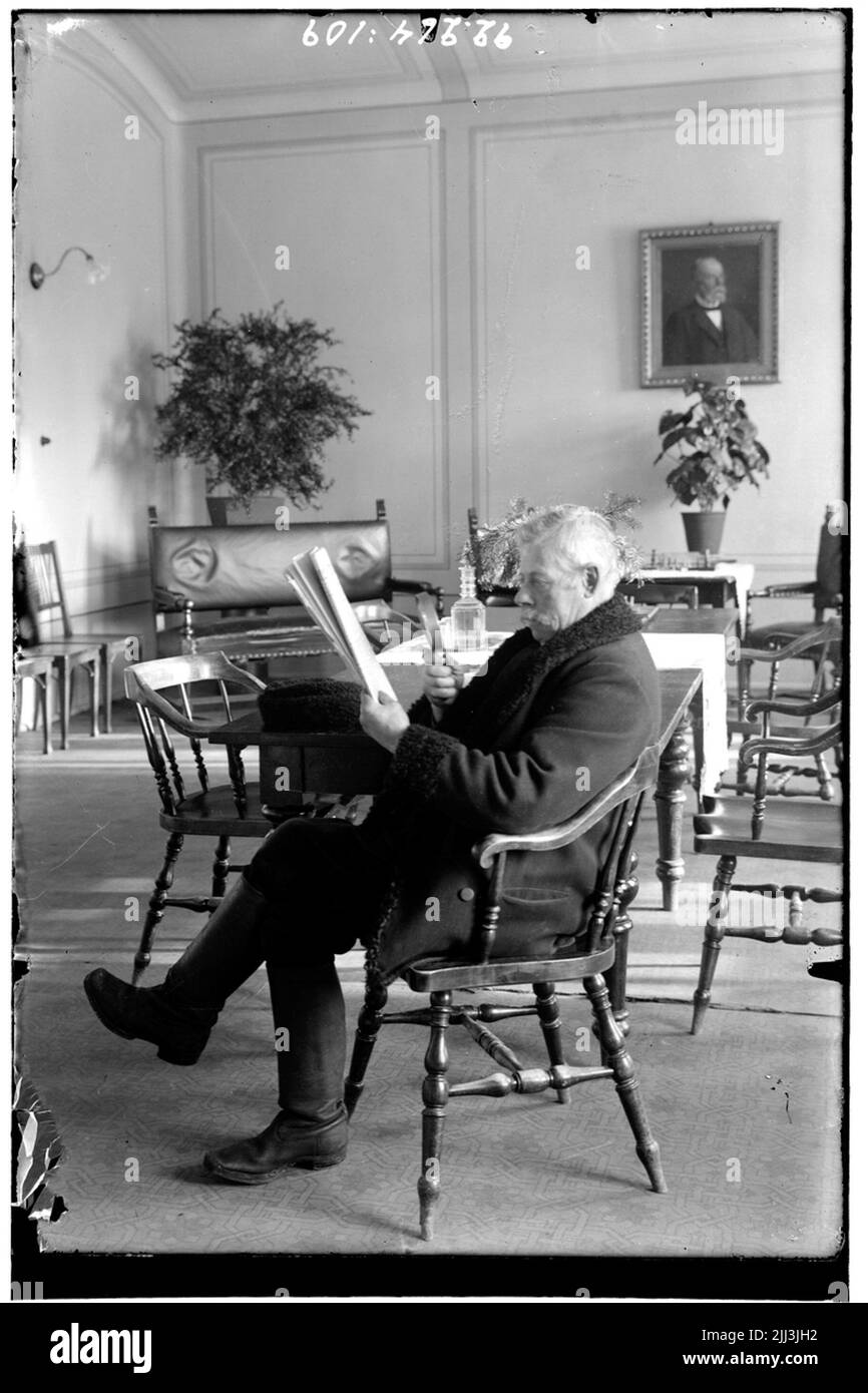 Hålahult sanatorium, interno, vecchio uomo siede e leggere il giornale con una lente d'ingrandimento, nella sala da pranzo? Vestito con cappotto invernale e stivali in pelle Foto Stock