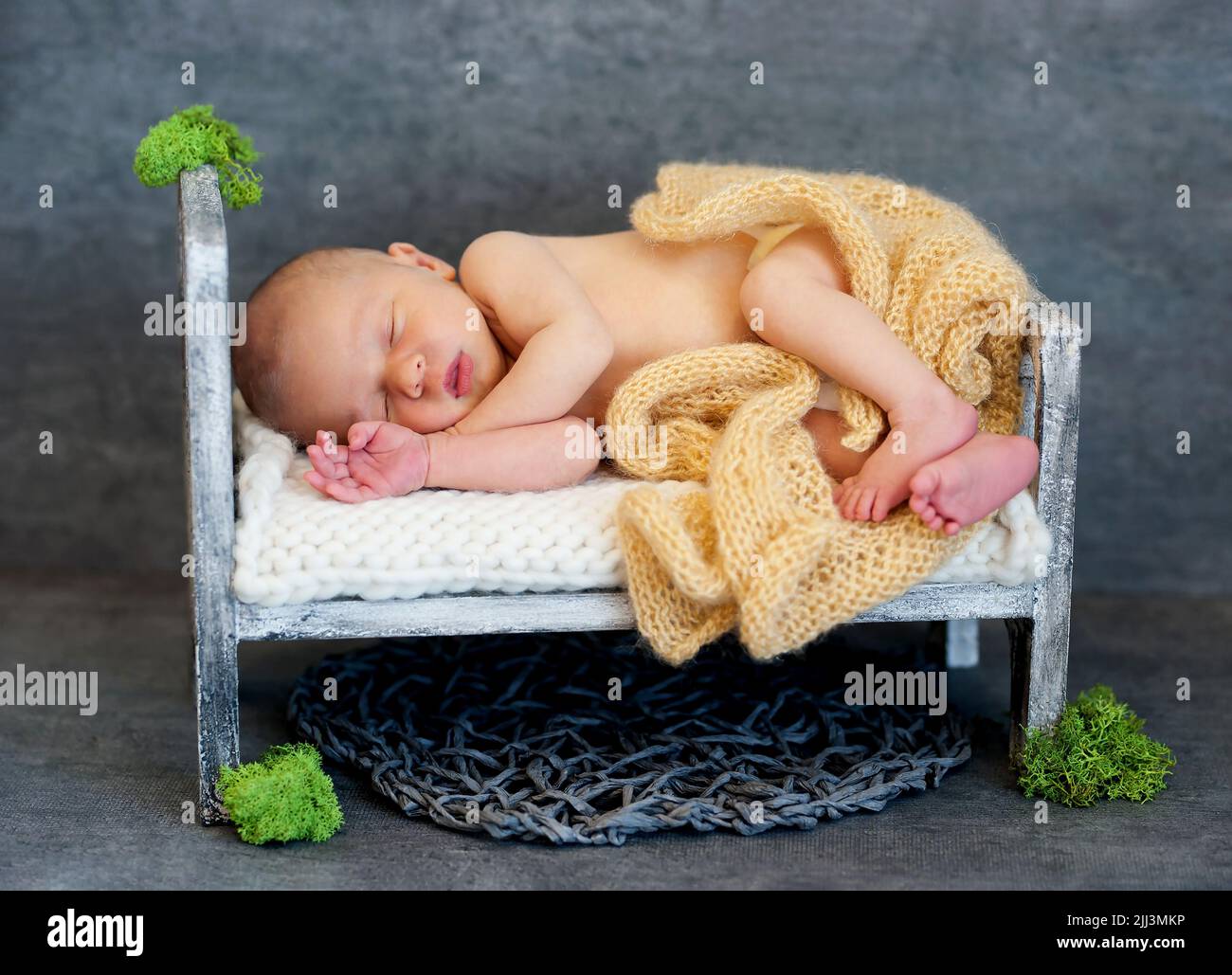 un bambino neonato dorme tranquillamente in una culla di legno con una coperta gialla Foto Stock