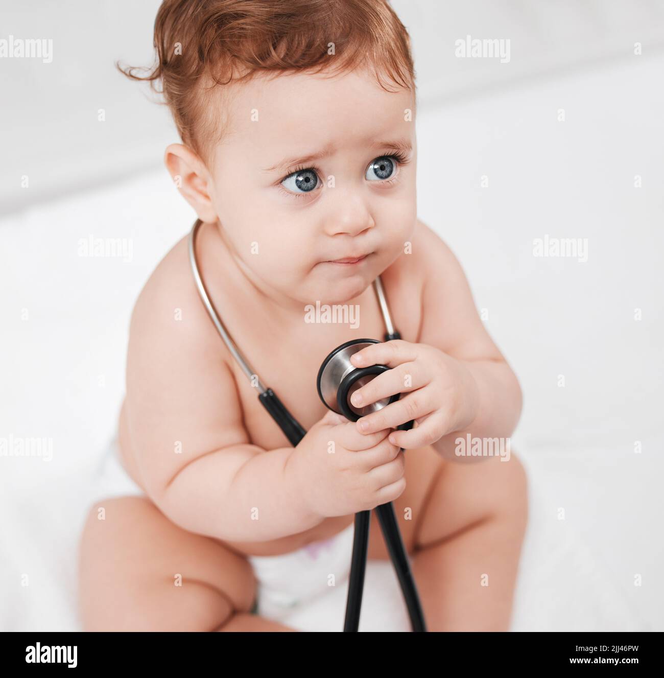 ERM, dottore signora questo ferirà. Un bambino adorabile tiene uno stetoscopio in una clinica durante il suo check-up. Foto Stock