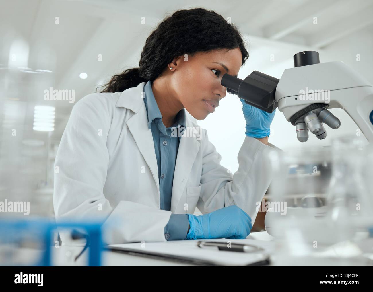 Lavorare senza distrazioni. Una giovane donna che usa un microscopio in un laboratorio scientifico. Foto Stock