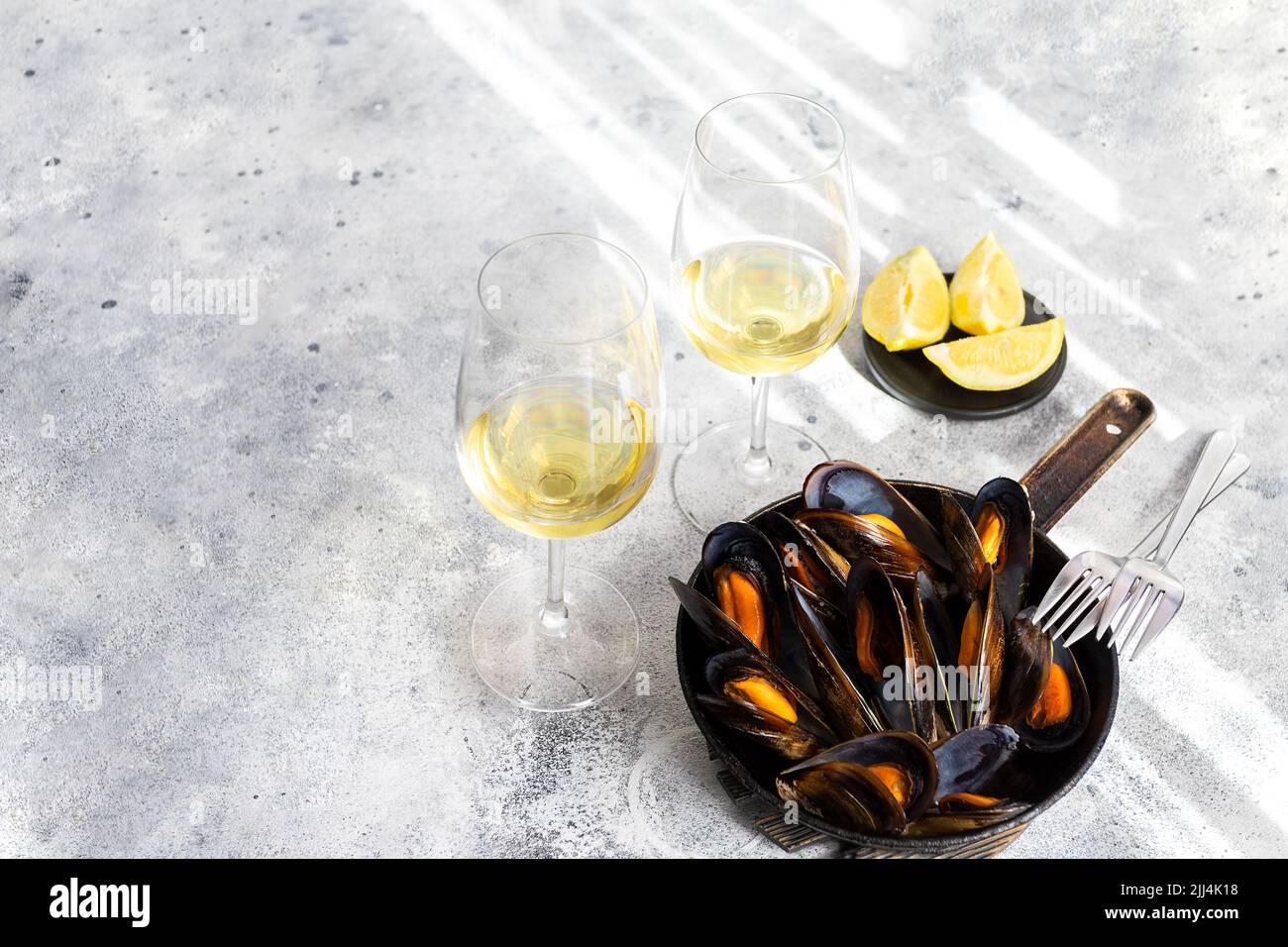 Cozze al vapore servite in padella, bicchieri di vino bianco su fondo cementizio. Popolare piatto di pesce mediterraneo sfondo. Spazio copia. Foto Stock