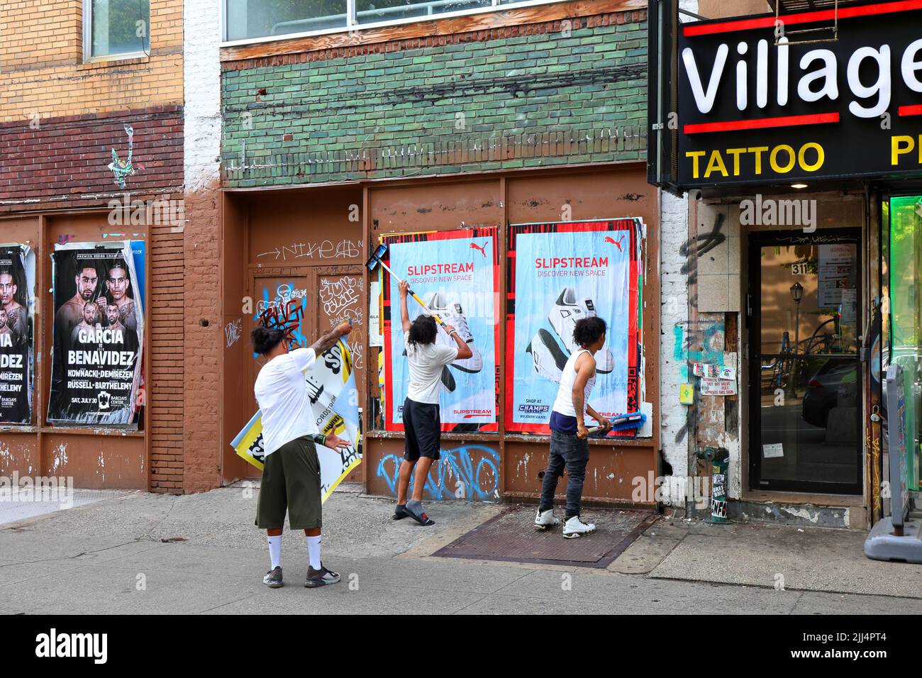Persone che sbatte poster pubblicitari su un muro, o pubblicità di pubblicazione selvaggia, come parte di una campagna di marketing urbano, a livello stradale, guerilla. Foto Stock