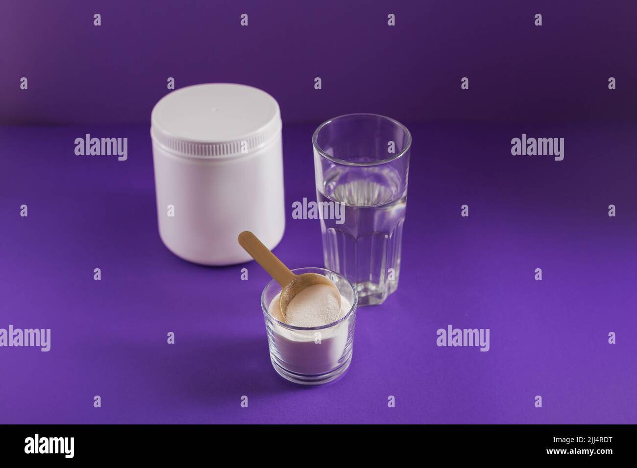 Vetro con collagene disciolto in acqua e collagene proteina polvere su tabella viola Foto Stock
