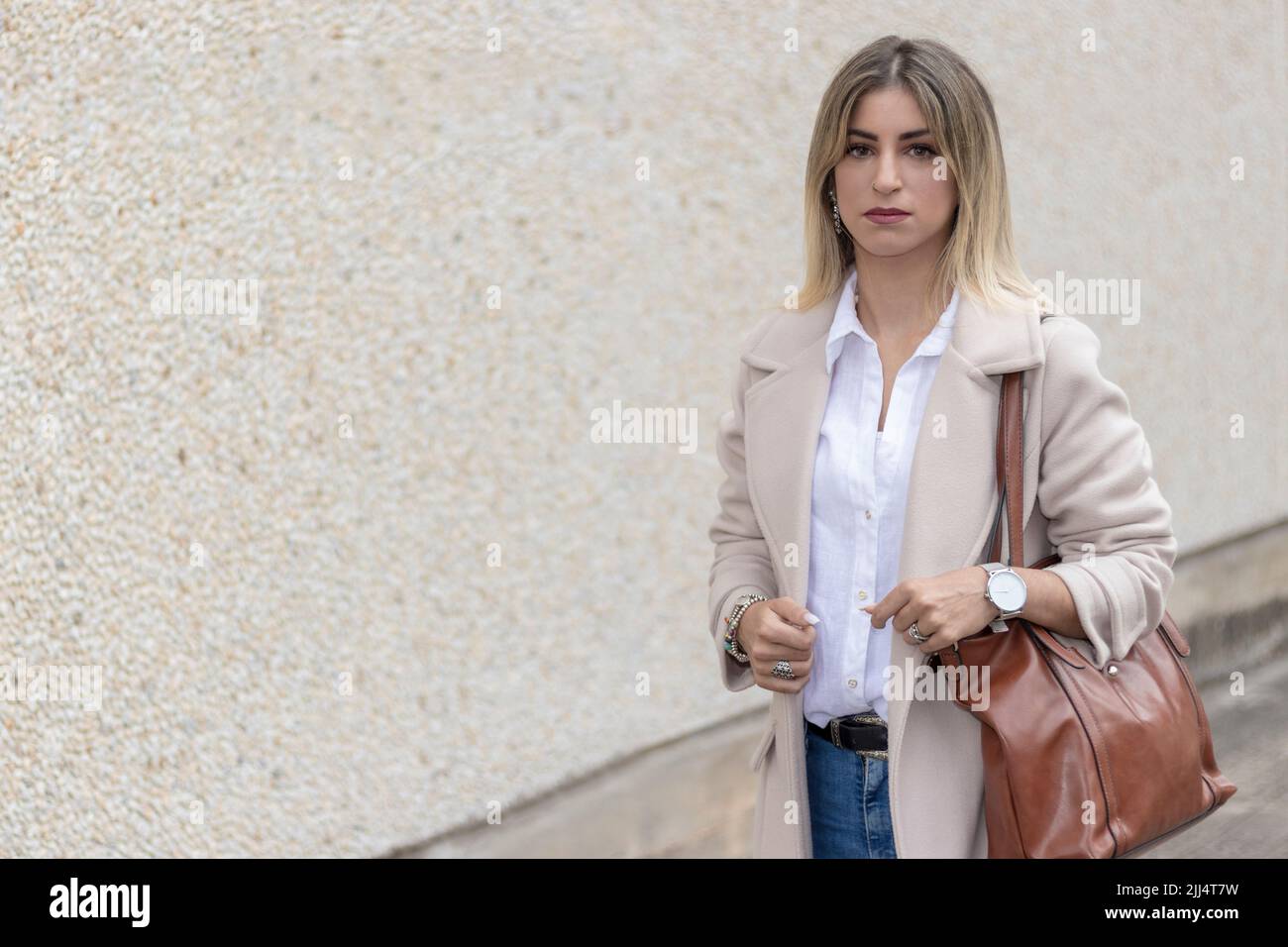donna business bionda per strada in un cappotto beige, camicia bianca e jeans Foto Stock