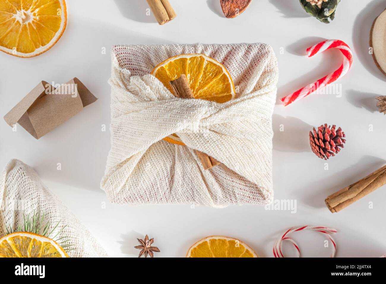 Zero spreco regalo di Natale. Mani che decorano i regali di natale in tessuto di lino con arance, ramo di abete verde su tavolo bianco. Regali Furoshiki. Foto Stock