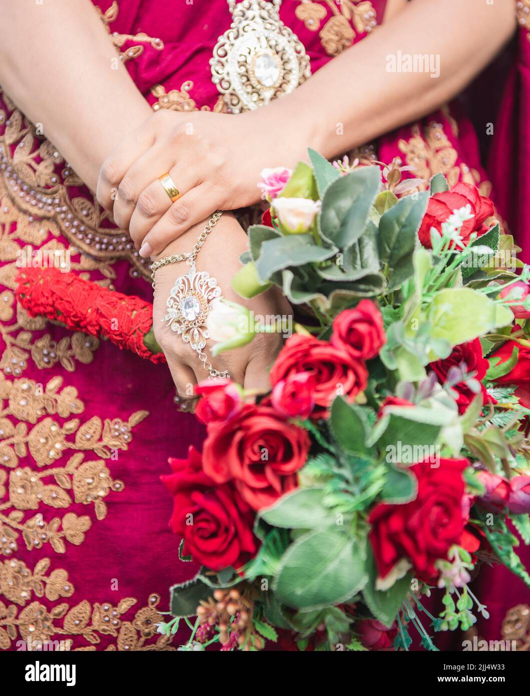 Sposa vestita di rosso che tiene una foto da vicino bouquet di fiori di rosa, bella casa sposa vestita con un sacco di gioielli d'oro. Concetto di più felice Foto Stock