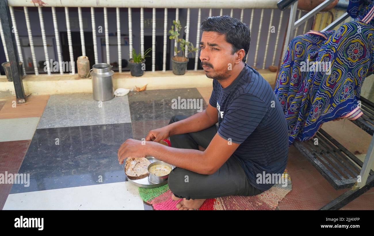 Ritratto di un bell'uomo affamato di mezza età seduto sul pavimento. Uomo indiano con cibo da asporto e bevande a casa Foto Stock