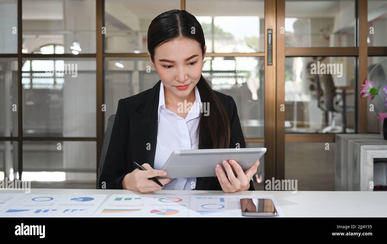 Donna d'affari pensata che utilizza un tablet digitale, analizzando i dati statistici online sul posto di lavoro Foto Stock