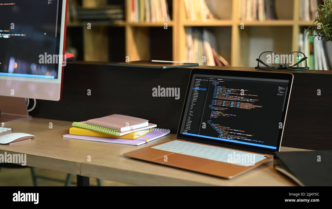 Computer portatile e pc su scrivania da ufficio in legno con codice di programmazione su schermi Foto Stock