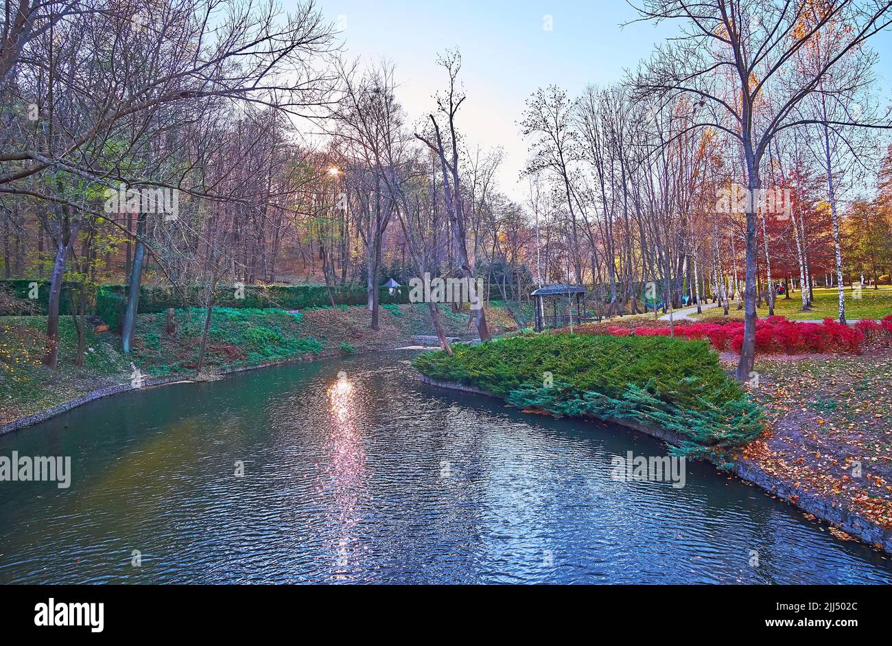Il tramonto sul piccolo fiume, circondato da alti alberi autunnali, arbusti di ginepro, Mezhyhirya, Ucraina Foto Stock