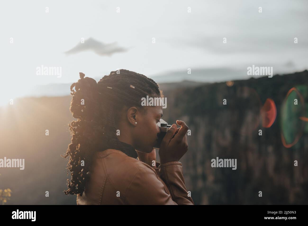 giovane donna turistica utilizzando una fotocamera retrò d'epoca. Giovane donna alla moda che scatta foto nella natura al tramonto Foto Stock