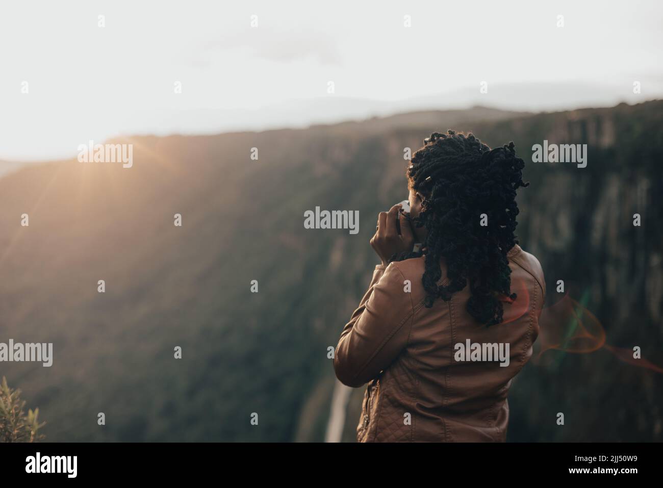 giovane donna turistica utilizzando una fotocamera retrò d'epoca. Giovane donna alla moda che scatta foto nella natura al tramonto Foto Stock