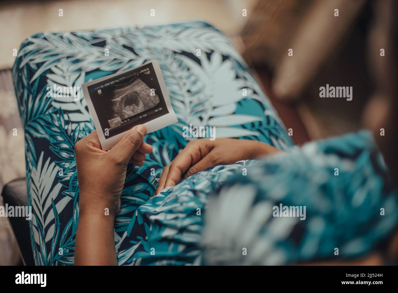 Una donna incinta seduta con un sonogramma seduta al chiuso Foto Stock