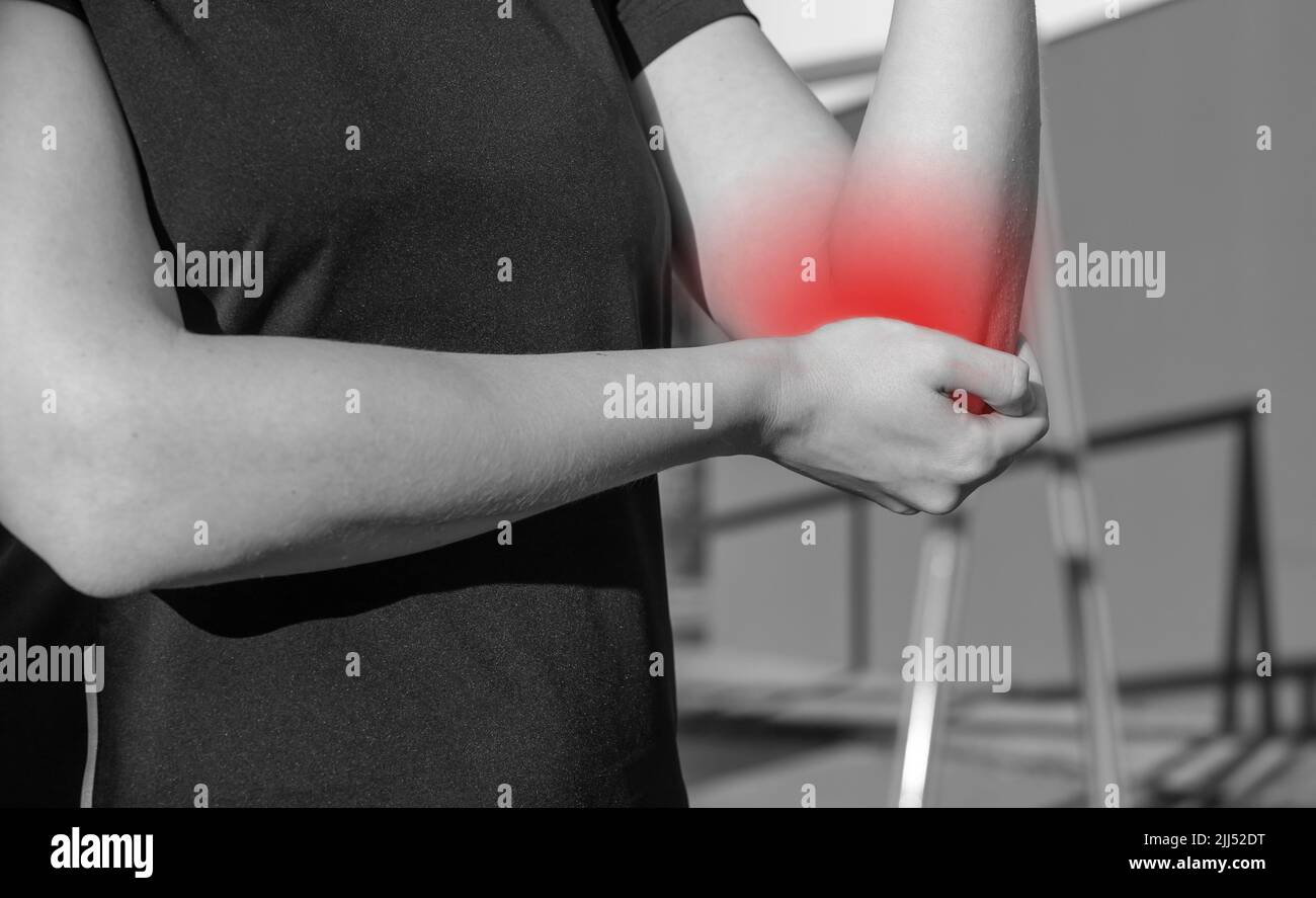 Dolore al gomito dell'atleta, trauma sportivo. Donna che tiene braccio doloroso con punto rosso. Ampie conseguenze sulla formazione. Concetto di problemi di salute. Bianco e nero. Foto di alta qualità Foto Stock