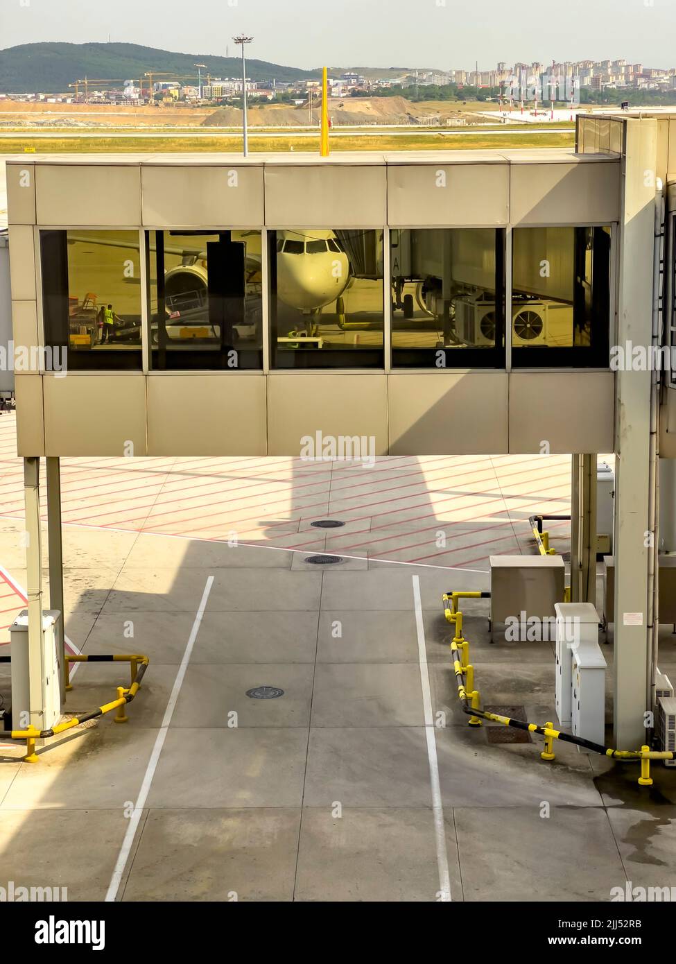 La vista frontale dell'aeroplano si riflette sulla finestra in vetro del ponte passerella passeggeri. Jetway collega l'aereo con il cancello d'imbarco del terminal dell'aeroporto. Ponte jet Foto Stock