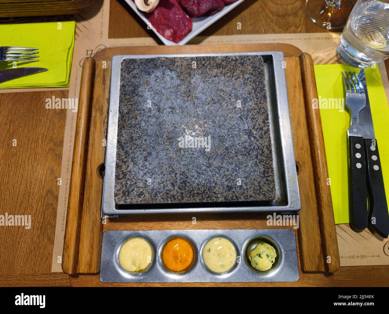 Pulire la griglia di pietra su un tavolo da ristorante con diversi tipi di salse sul fondo. La gente può mettere la propria carne sulla griglia Foto Stock